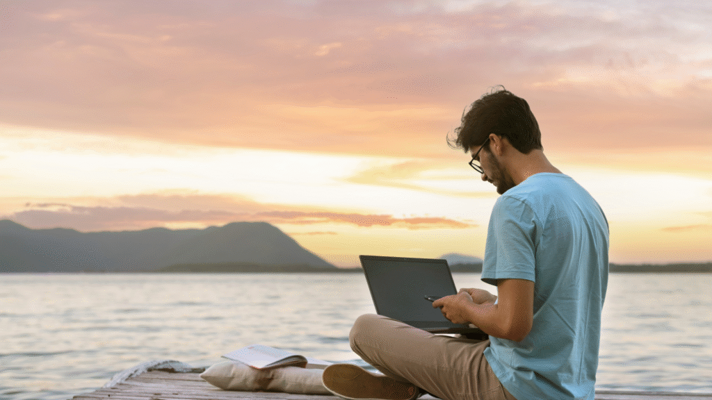 Digital nomad working on a laptop at the beach during sunset, enjoying remote work freedom and eco-friendly travel lifestyle