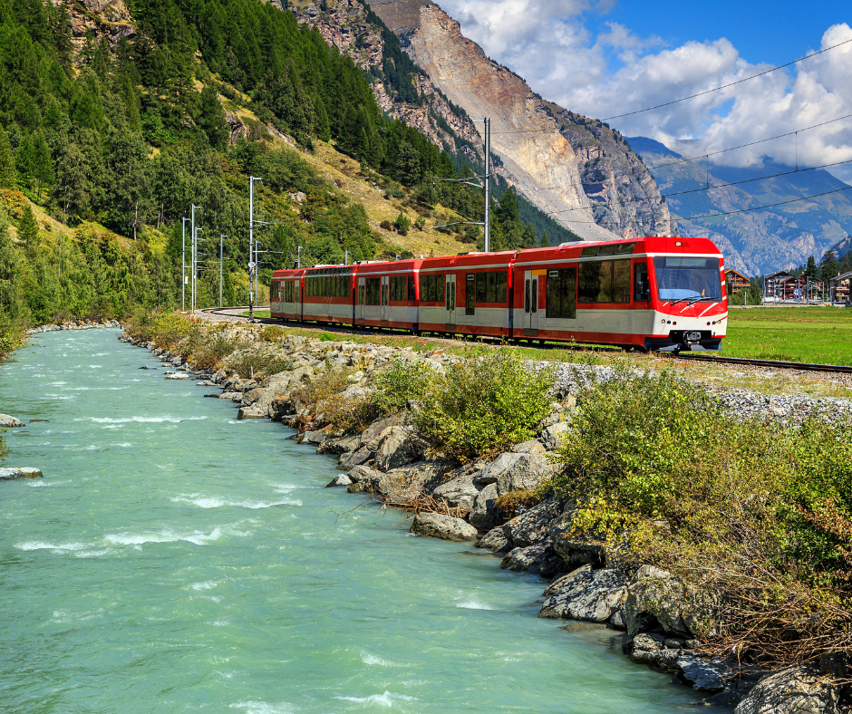 Scenic slow train passing a creek and forested mountainside