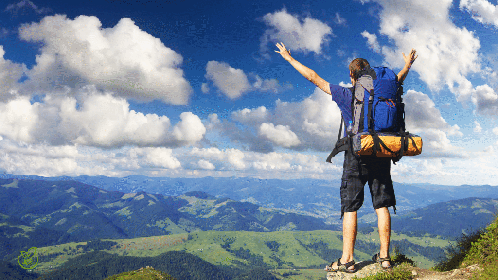 Hiker standing on a mountain peak with arms outstretched — ecotourism adventure highlighting sustainable tourism, responsible tourism, and eco friendly travel in wild nature