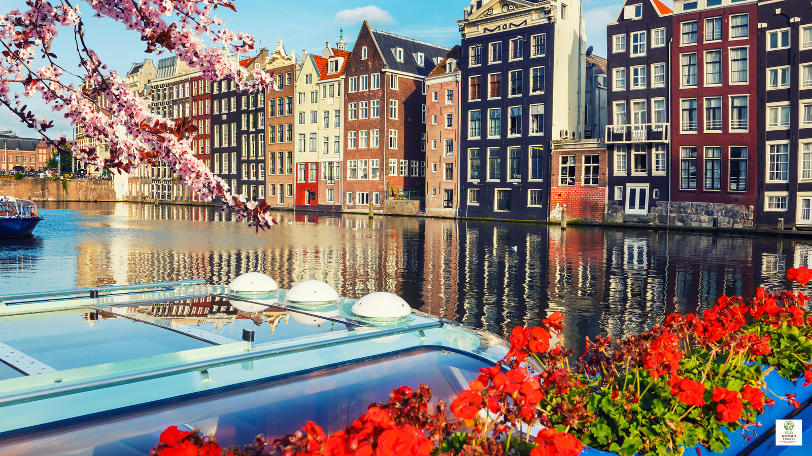Colorful historic buildings along an Amsterdam canal with bikes and calm water, representing eco city hotels and basecamps.