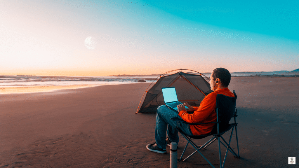 Digital nomad working on a laptop at sunset on a quiet beach, representing sustainable remote work in 2025