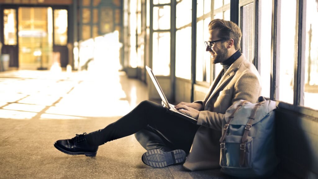 Man working on a laptop by a station window while planning a digital nomad Europe train itinerary