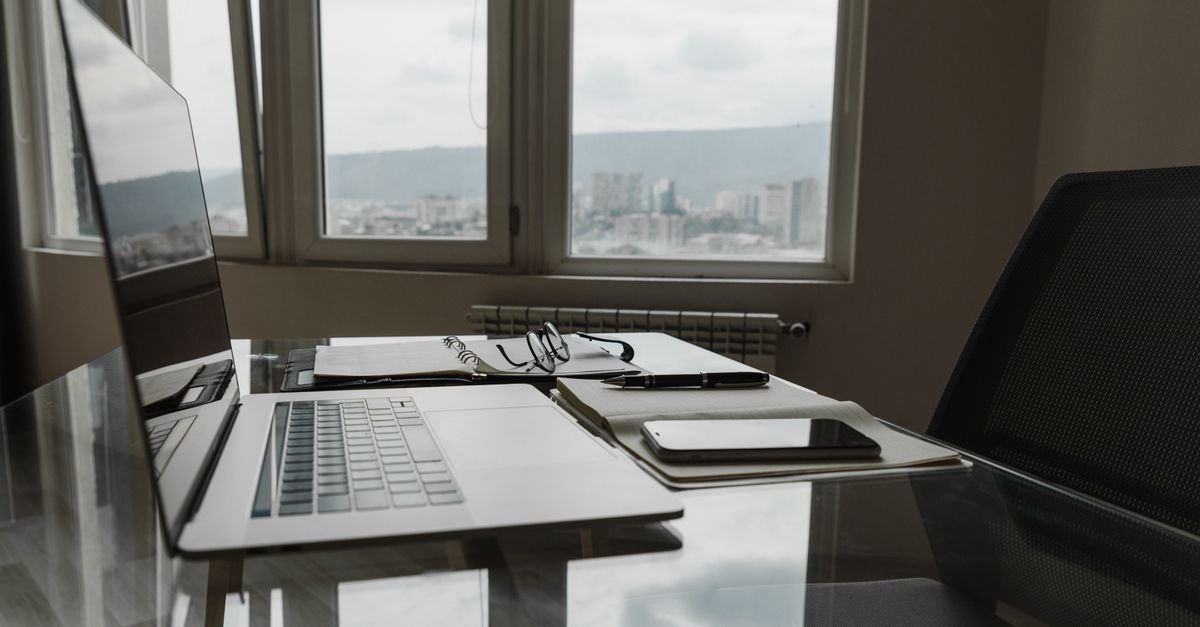 A laptop and notebook on a desk beside a window